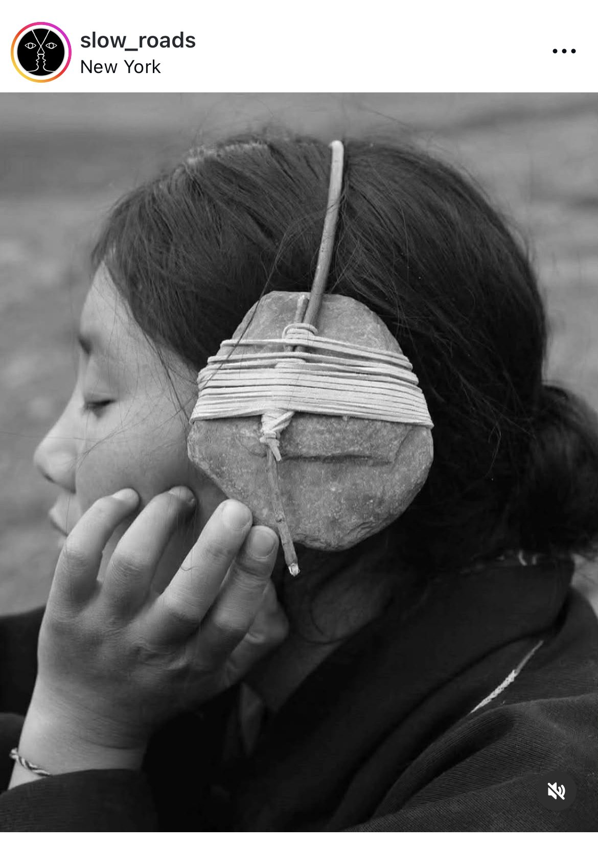 Black and white image of a girl wearing mock headphones made of sticks, string, and stone.