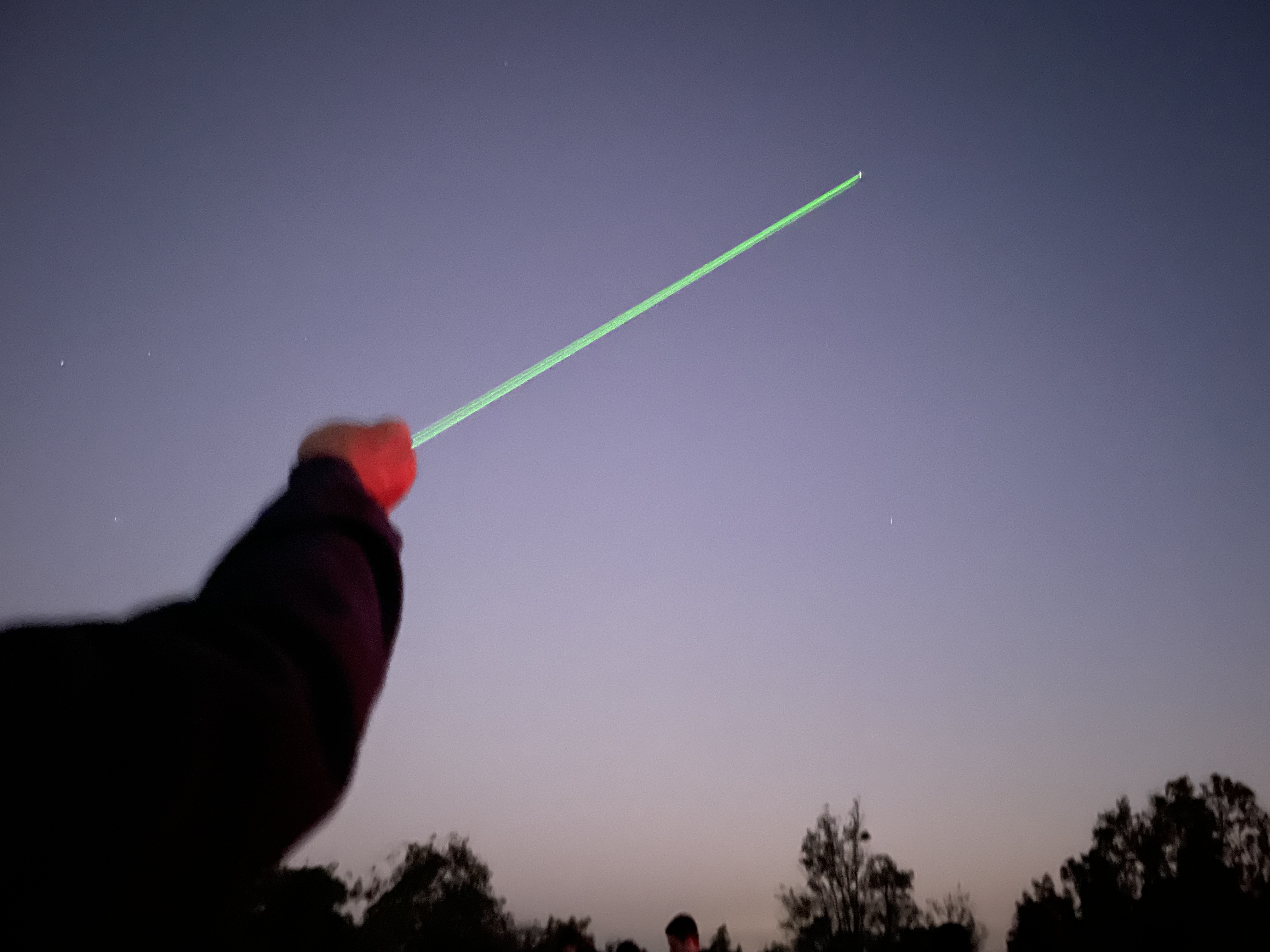Outstretched red arm pointing a green laser at Saturn during a stargazing event