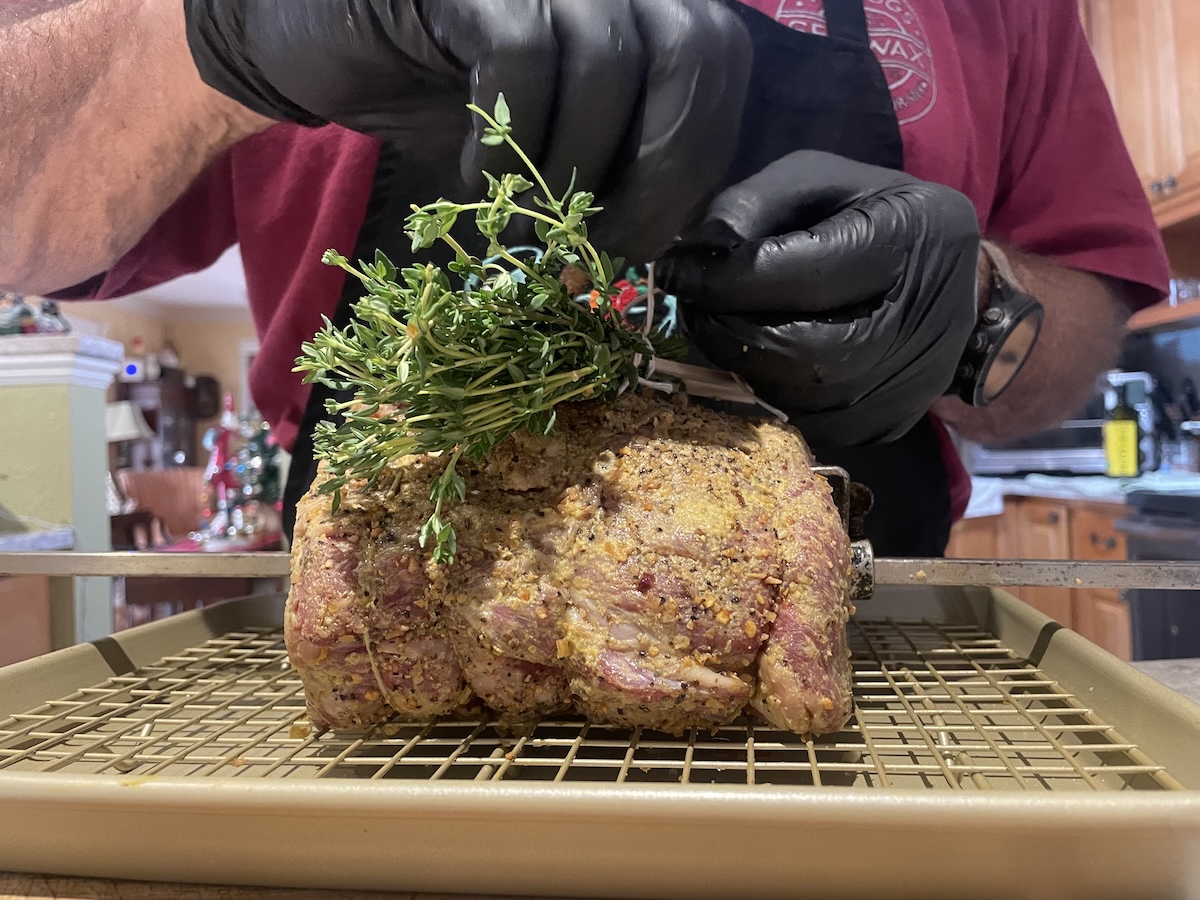 Large ribeye roast on a rotisserie rod with rosemary and thyme